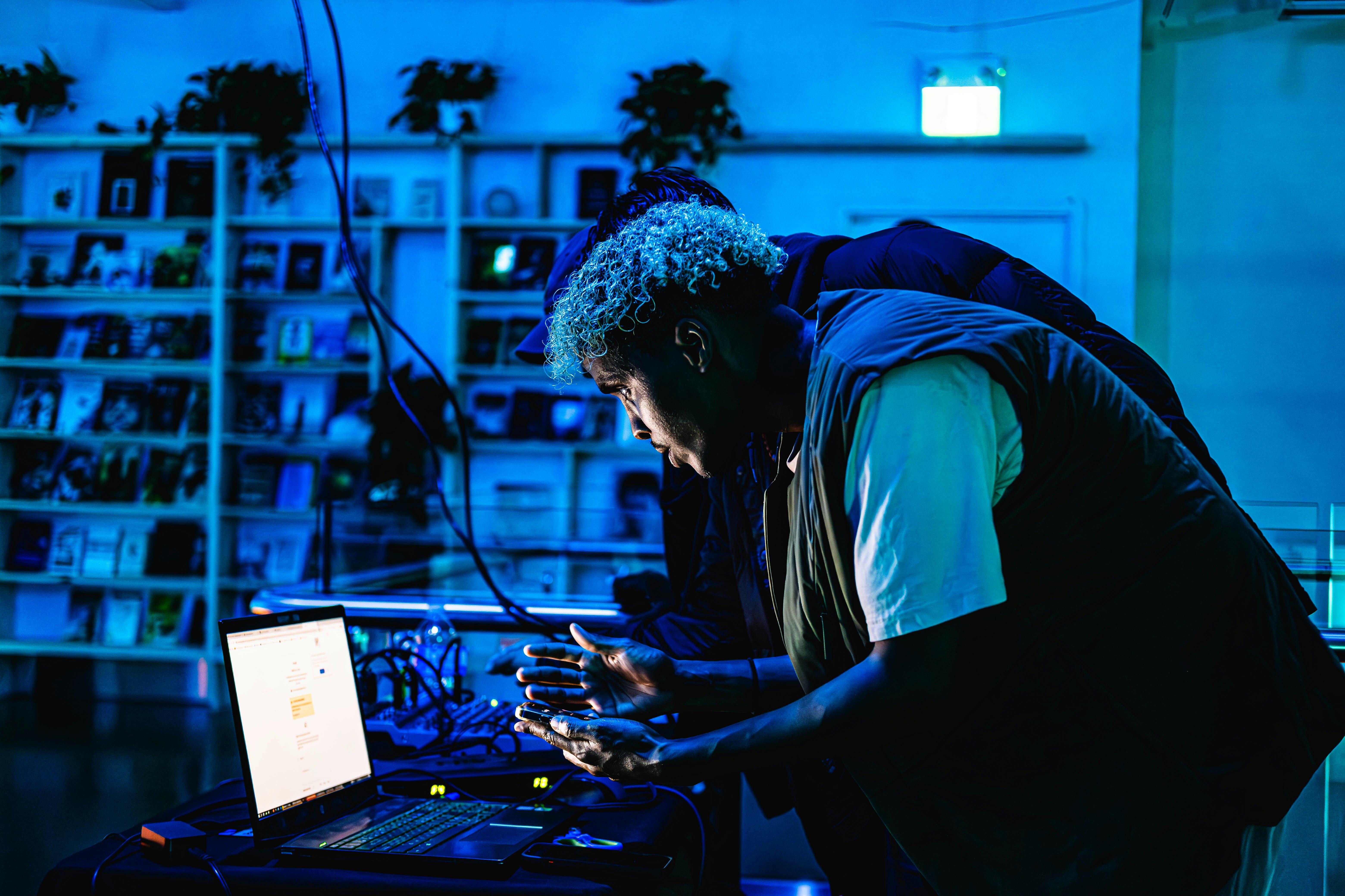 Artist leaning over laptop in blue-lit studio